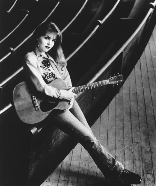 Black and White photo of Joy Lynn White sitting with her guitar on her hand and legs stretched.